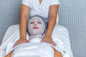 Beautician applying a towel to the shoulders and neck of a woman who is covered her face with gauze for skin treatment photo