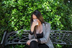 Female with pollen allergy blowing nose near bush photo