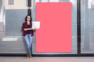 Woman standing while using a laptop next to a shop window photo
