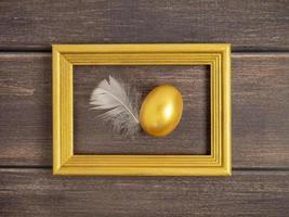 Stylish concept of Easter golden eggs. Easter golden egg in golden frame on dark wooden background with copy space photo