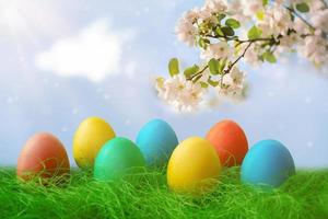 contento Pascua de Resurrección. un fila de decorativo Pascua de Resurrección huevos en el verde césped. en el antecedentes de el cielo y manzana árbol flores foto