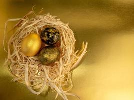 Three Easter eggs, painted gold and black, lie in a nest on a sparkling background photo