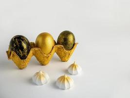 Easter eggs painted in gold and black in a textured stand on a white background with meringues photo