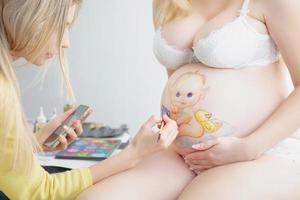 Makeup artist paints a small child on the belly photo