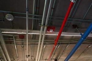 Tuberías de sistema sanitario y cables eléctricos instalados bajo estructura de hormigón armado de losa plana en edificio. Tuberías de ventilación en estacionamiento subterráneo foto