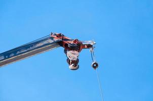 Mobile crane boom with hook hanging by wire cable background blue sky,close up photo