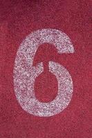 Number six on running track. White track number on red rubber racetrack, texture of running racetracks in stadium photo