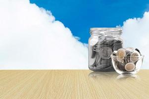 coins in a glass jar on Wood floor ,savings coins - Investment And Interest Concept saving money concept, growing money on piggy bank. isolated on blue sky background photo