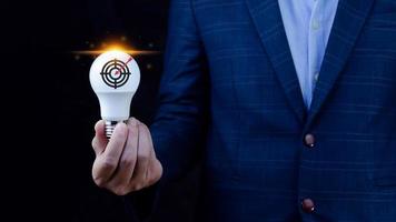 Businessman holding light bulb for concept new idea with virtual dartboard and arrow with copy space for setup business objective target concept. photo