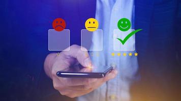 Customer service evaluation concept feedback rating and positive customer review experience, using a smartphone And pressing face emoticon smile in satisfaction on virtual touch screen photo