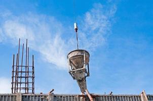 cemento o hormigón Cubeta colgando en cable a construcción sitio con azul cielo antecedentes foto