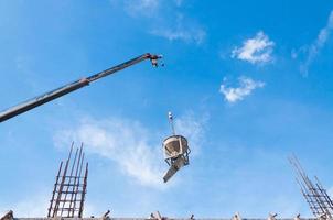 Cement or concrete bucket hanging on wire at construction site with blue sky background photo