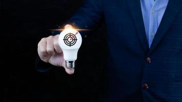 Businessman holding light bulb for concept new idea with virtual dartboard and arrow with copy space for setup business objective target concept. photo