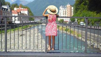 niña con sombrero en el terraplén de un río de montaña en una ciudad europea. video