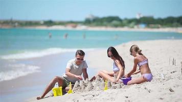 padre e bambini fabbricazione sabbia castello a tropicale spiaggia. famiglia giocando con spiaggia giocattoli video