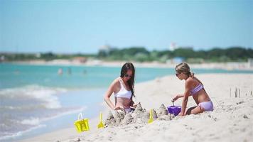 Family of mom and girl making sand castle at tropical white beach video