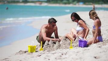 vader en kinderen maken zand kasteel Bij tropisch strand. familie spelen met strand speelgoed video
