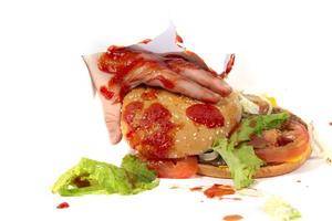 A hand holds a hamburger against the background of splashed ketchup on a white background.Creative hamburger. photo