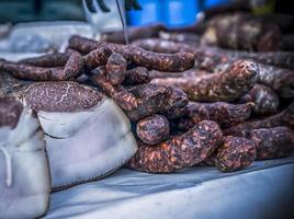 An outdoor stall with dried sausages and bacon being sold photo