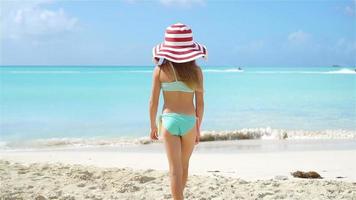 adorable pequeño niña en grande sombrero caminando a lo largo blanco arena playa video