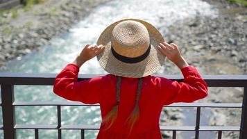 niña con sombrero en el terraplén de un río de montaña en una ciudad europea. video