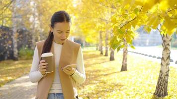 Fall concept - beautiful woman drinking coffee in autumn park under fall foliage video