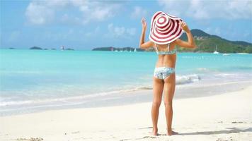 adorable pequeño niña en grande sombrero caminando a lo largo blanco arena playa video