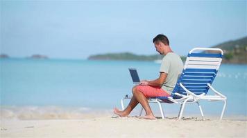 jovem com computador tablet durante as férias na praia tropical video