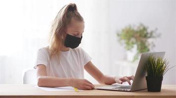 Serious schoolgirl sitting at table with laptop and textbook and doing homework. video