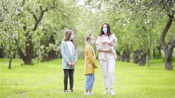 Family of mother and daughters in blooming cherry garden in masks