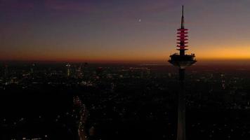 Drönare video av en flyga förbi av de frankfurt tv torn i de kväll under en färgrik solnedgång med de frankfurt horisont i de bakgrund