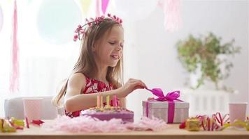 une fille caucasienne sourit rêveusement et regarde le gâteau arc-en-ciel d'anniversaire. fond coloré festif avec des ballons. fête d'anniversaire et concept de souhaits. video