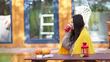 Happy young woman with phone and drinking coffee sitting at the wooden table outdoors video