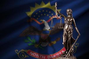 North Dakota US state flag with statue of lady justice and judicial scales in dark room. Concept of judgement and punishment photo