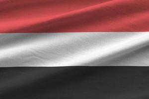 Yemen flag with big folds waving close up under the studio light indoors. The official symbols and colors in banner photo