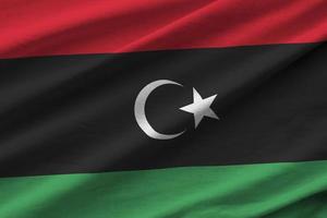 Libya flag with big folds waving close up under the studio light indoors. The official symbols and colors in banner photo