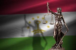 Tajikistan flag with statue of lady justice and judicial scales in dark room. Concept of judgement and punishment photo