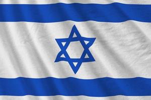 Israel flag with big folds waving close up under the studio light indoors. The official symbols and colors in banner photo