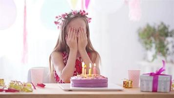 Caucasian girl is dreamily smiling and looking at birthday rainbow cake. Festive colorful background with balloons. Birthday party and wishes concept. video