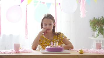 une fille caucasienne sourit rêveusement et regarde le gâteau arc-en-ciel d'anniversaire. fond coloré festif avec des ballons. fête d'anniversaire et concept de souhaits. video