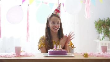 kaukasisches mädchen lächelt träumerisch und betrachtet geburtstagsregenbogenkuchen. festlicher bunter hintergrund mit luftballons. geburtstagsfeier und wunschkonzept. video