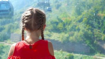 Adorable happy little girl in the cabin on the cable car in mountains in the background of beautful landscape video