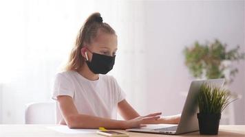 Serious schoolgirl sitting at table with laptop and textbook and doing homework. video