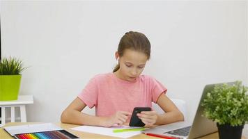 Serious schoolgirl sitting at table with laptop and textbook and doing homework. Study from home video