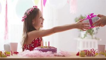 kaukasisches mädchen lächelt träumerisch und betrachtet geburtstagsregenbogenkuchen. festlicher bunter hintergrund mit luftballons. geburtstagsfeier und wunschkonzept. video