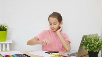 grave Chica de escuela sentado a mesa con ordenador portátil y libro de texto y haciendo tarea. estudiar desde hogar video