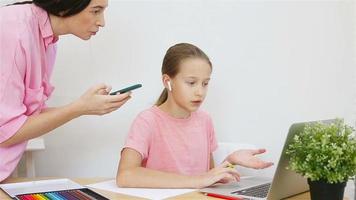 wenig Mädchen studieren beim Zuhause beim das Computer. Mutter hilft ihr Tochter mit ihr Aufgaben. online Ausbildung. Kind studieren beim Zuhause im Quarantäne video