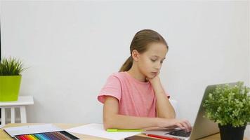 grave Chica de escuela sentado a mesa con ordenador portátil y libro de texto y haciendo tarea. estudiar desde hogar video