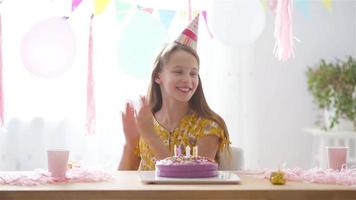 caucasian flicka är drömmande leende och ser på födelsedag regnbåge kaka. festlig färgrik bakgrund med ballonger. födelsedag fest och lyckönskningar begrepp. video