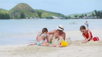 padre y dos niñas jugando con arena en la playa tropical
